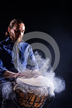 Man playing on djembe drum with white powder.