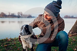 Man playing with dog in autumn park by lake. Happy pet having fun outdoors