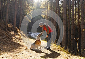 Man playing with dog in forest lit by sunlight. Autumn season.