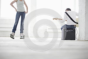 Man Playing Electric Guitar With Woman Wearing Inline Skate In W