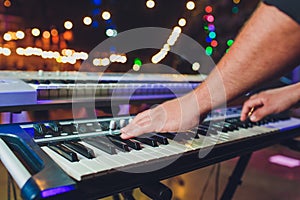 Man playing electronic musical keyboard synthesizer by hands on white and black keys in recording studio.