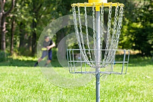 Man playing flying disc sport game in the park, chain basket in the focus
