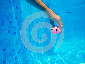 Man playing with generic rubber fish toy in swimming pool
