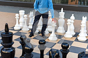 Man playing gigantic chess outdoors. Outdoor chess board with big plastic pieces. Giant size chess in public area zone. Close up