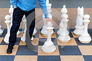 Man playing gigantic chess outdoors. Outdoor chess board with big plastic pieces. Giant size chess in public area zone. Close up