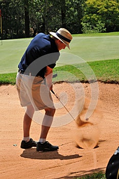 Man playing golf shot out of sand bunker on green