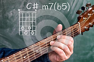 Man playing guitar chords displayed on a blackboard, Chord C minor 7b5