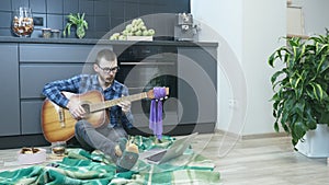 Man playing guitar at kitchen in self isolation. Caucasian young male learning to play acoustic guitar with online teacher. Man tr