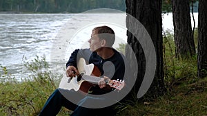 Man Playing Guitar by the River in the Evening