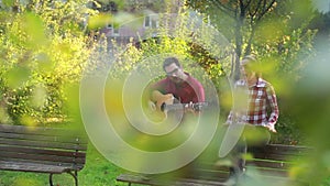 Man playing guitar and singing with woman while sitting on park bench