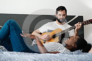 Man Playing Guitar And Woman Singing Song In Bedroom