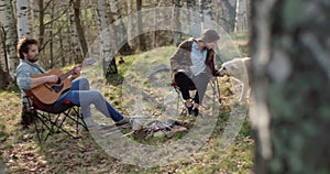 Man playing guitar and woman stroking dog together around fire place.real friends people outdoor camping tent vacation