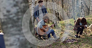 Man playing guitar and woman stroking dog together around fire place.real friends people outdoor camping tent vacation