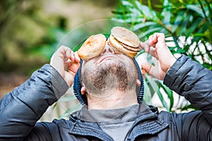 Man playing with his food - placing his hamburgers on his face - front view