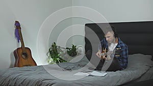 Man playing solo on electric guitar. Male guitar player performing solo part at home sitting on bed. Musician emotionally performs