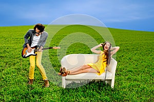 Man playing a solo on the guitar with girl lying on the couch