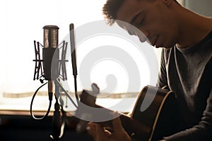 Man playing spanish guitar and singing while recording it with a microphone. Home studio