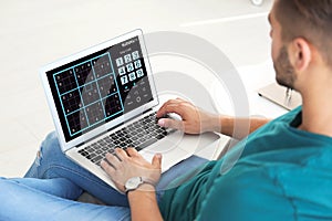 Man playing sudoku game on laptop indoors, closeup