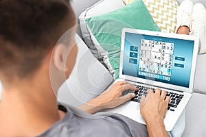 Man playing sudoku game on laptop indoors, closeup