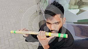 Man playing a traditional bamboo flute outdoors near a vehicle focused and practicing musical art