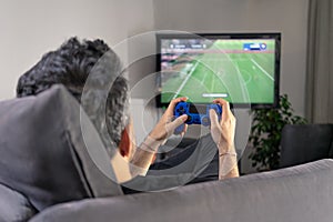 Man playing video game at home sitting on coach sofa in front of television with play game concole and joystick in hands