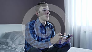 Man playing video games on console while sitting on couch in front of TV. Young excited man plays online video game using wireless