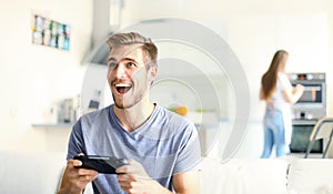 Man playing video games while his girlfriend cooking in the kitchen.