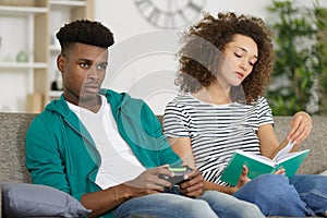 man playing video games while woman reading book
