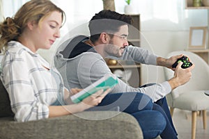 man playing video games while women reads book at home