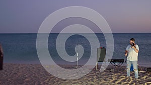 A man is playing the violin at the seaside standing on sand during sunsent.