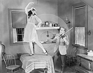 Man playing violin for woman dancing on table