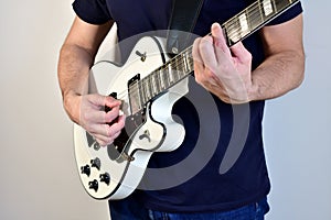 Man playing a white electric guitar with humbucker pickups.