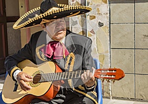 Man plays acoustic guitar while dressed in traditional  Mariachi  suit