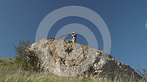 A man plays the Australian Aboriginal musical instrument Didgeridoo on a rock ledge against a blue sky. View from bottom
