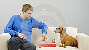 A man plays chess with a dachshund.