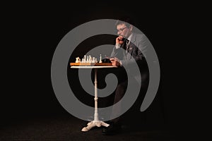 A man plays chess and smokes a pipe on a dark background