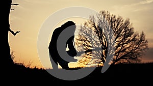 Man plays electric guitar and sings a lyric song in a field near the tree at sunset. silhouette