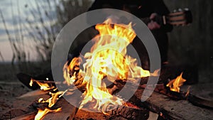 A man plays the guitar. In the foreground is a fire. Summer evening. Slow motion