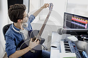 Man plays guitar and produce electronic soundtrack or track in project at home. Male music arranger composing song on