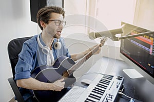 Man plays guitar and singing and produce electronic soundtrack or track in project at home. Male music arranger