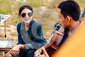 A man plays a guitar for a woman while camping beside the lake