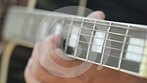 A man plays music on an acoustic guitar in the garden. Plays chords on the strings with his fingers. Close-up of a hand