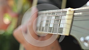 A man plays music on an acoustic guitar in the garden. Plays chords on the strings with his fingers. Close-up of a hand