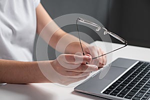 Man plays nervously with eyeglasses working at laptop
