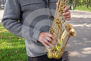 Man plays on saxophone in the park. Street musician with sax performs music for charity. Public solo performance by wind