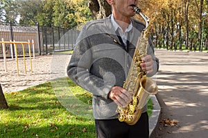 Man plays on saxophone in the park. Street musician with sax performs music for charity. Public solo performance by wind