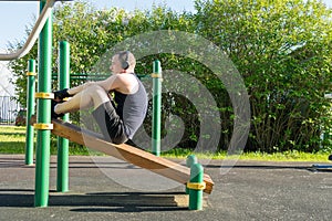 A man plays sports on the site, does exercises to strengthen the press using an inclined bench