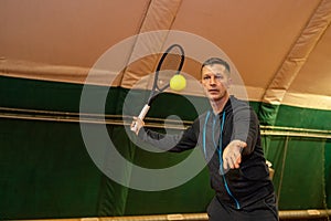 man plays tennis with a racket and a ball on an indoor court with a net.