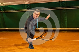 man plays tennis with a racket and a ball on an indoor court with a net.