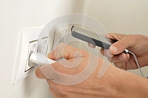 Man plugging in the plug of his smpartphone in a socket